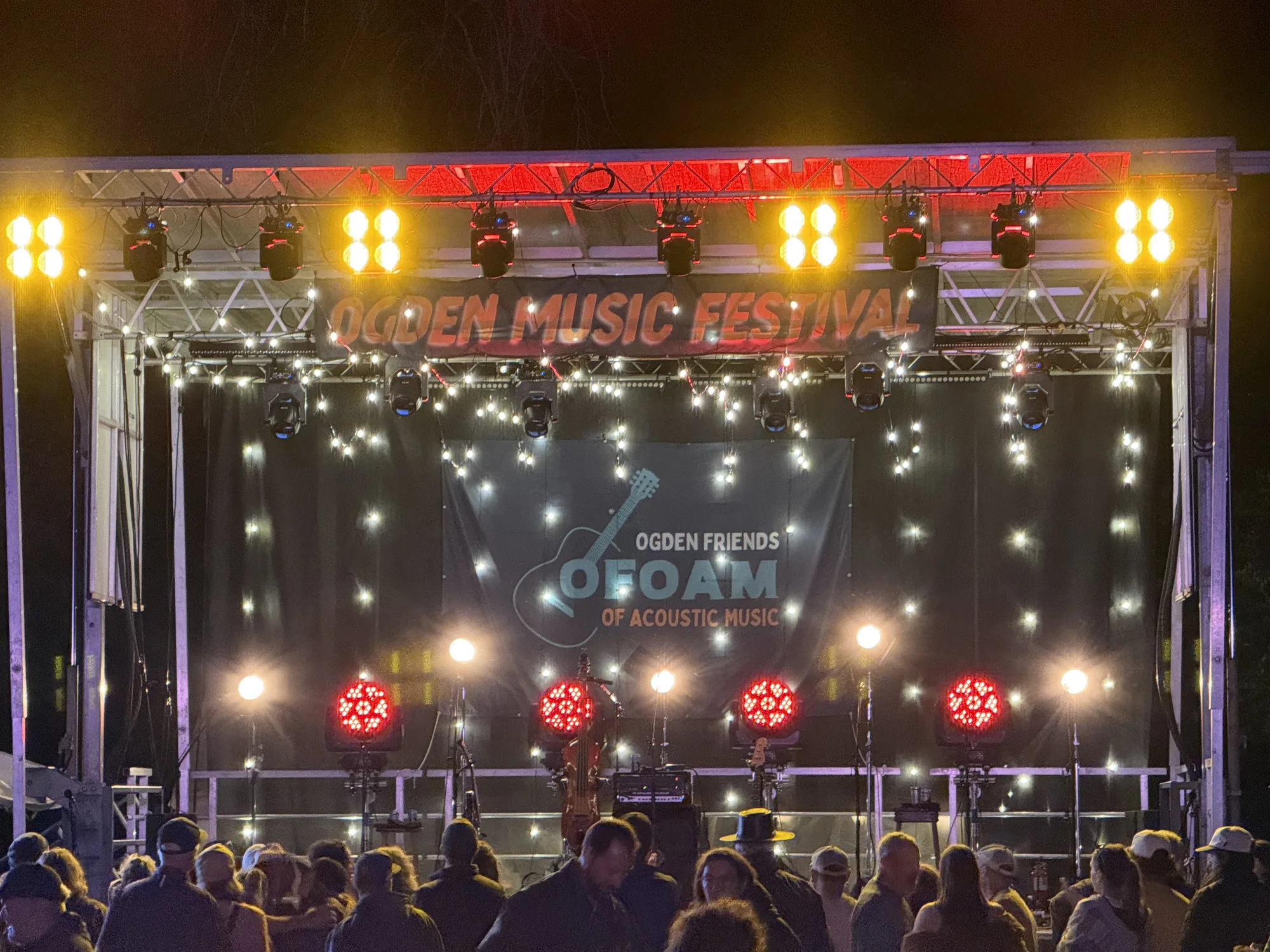 Audience in front of the OFOAM outdoor stage with red and amber lights and strings of white bulbs
